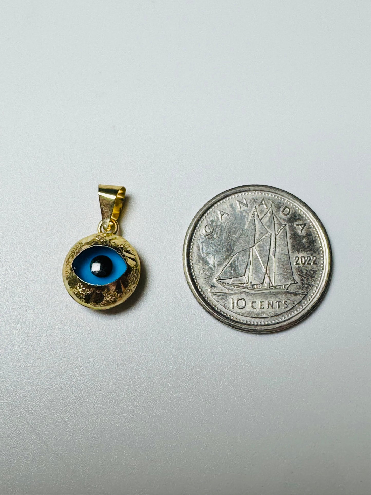 Pendentif 3e œil rond en or 10K comparé à une pièce de 10 cents
